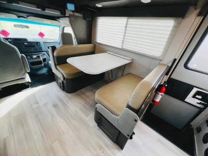 RV rental interior: cozy dinette with white table, comfortable benches, light wood flooring, and front cab view.. Forest River Coachmen Leprechaun 2023