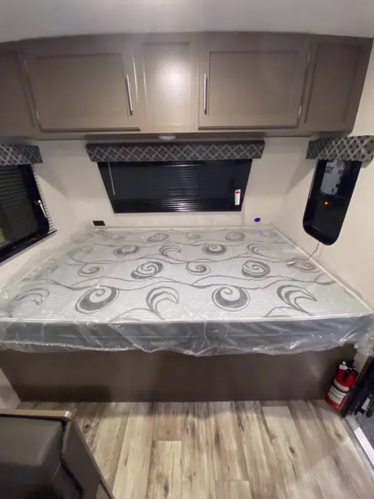 Clean RV rental bedroom with a new bed in plastic, overhead storage, and windows.. KZ Sportsmen Classic 180BH 2024