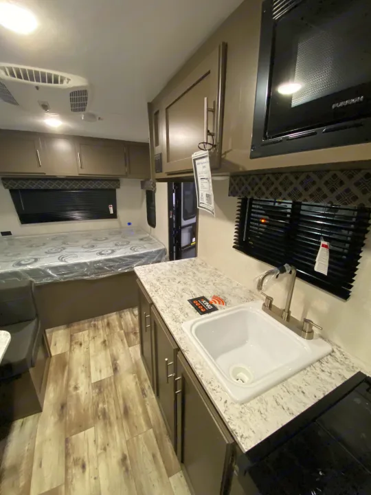 RV rental interior: kitchen (sink, microwave), bench seating, bed, and AC unit. Ready for travel comfort.. KZ Sportsmen Classic 180BH 2024