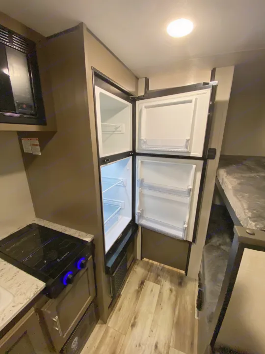 RV rental's practical kitchen: open refrigerator, microwave, stove, and adjacent bunk beds.. KZ Sportsmen Classic 180BH 2024