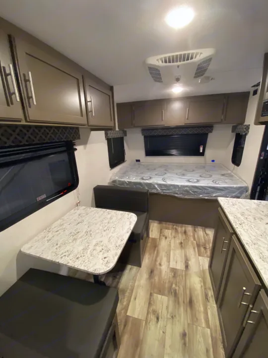 Explore this RV rental's cozy interior: bed, dinette, overhead cabinets, and wood-look flooring. Perfect for adventures.. KZ Sportsmen Classic 180BH 2024