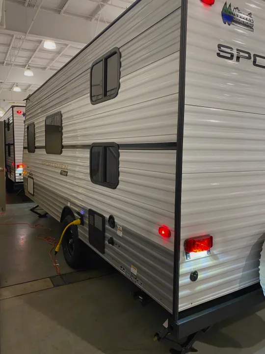 Indoor view of an RV rental: a grey travel trailer with windows and red rear lights, plugged into power.. KZ Sportsmen Classic 180BH 2024