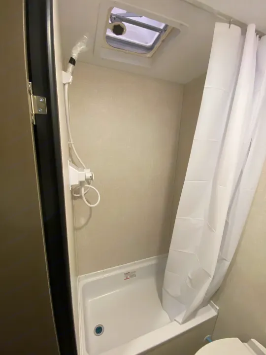 RV rental's compact bathroom features a white shower curtain, tub, handheld shower, and ceiling vent.. KZ Sportsmen Classic 180BH 2024
