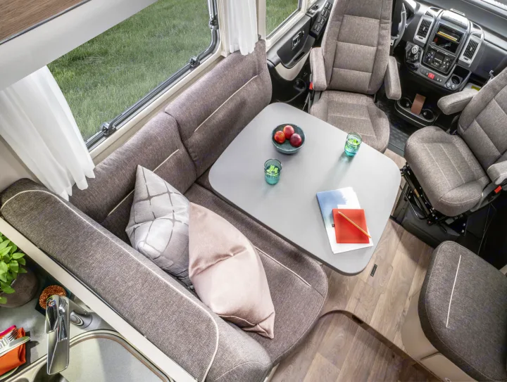 Modern RV rental interior with inviting dining lounge, compact kitchen, and swiveling front seats. Enjoy comfortable travels.. Hymer Exis I 678 2024