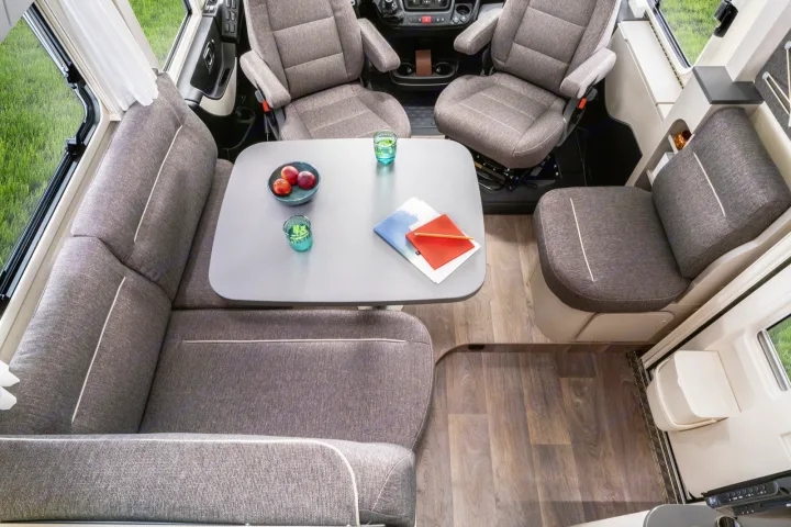 Cozy RV rental interior: a spacious dining area with an L-shaped sofa, swiveling front seats, and wood flooring.. Hymer Exis I 678 2024