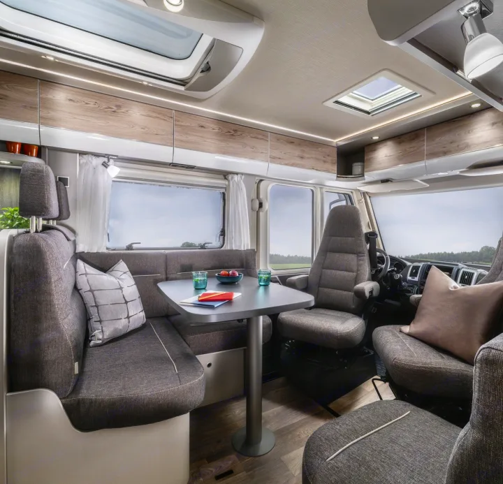 Spacious RV rental interior: A modern motorhome dining area with booth seating, swivel chairs, and large windows.. Hymer Exis I 678 2024
