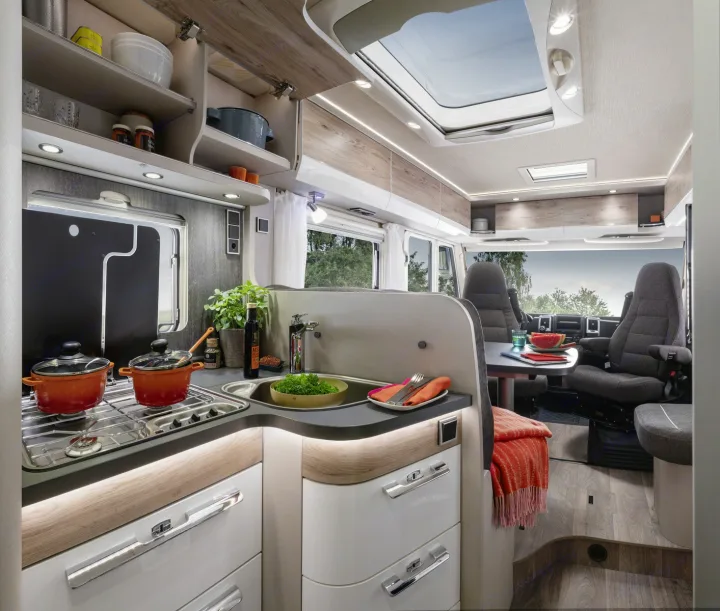 Spacious, modern RV rental interior featuring a bright kitchen with stove and sink, plus a comfortable dining area.. Hymer Exis I 678 2024