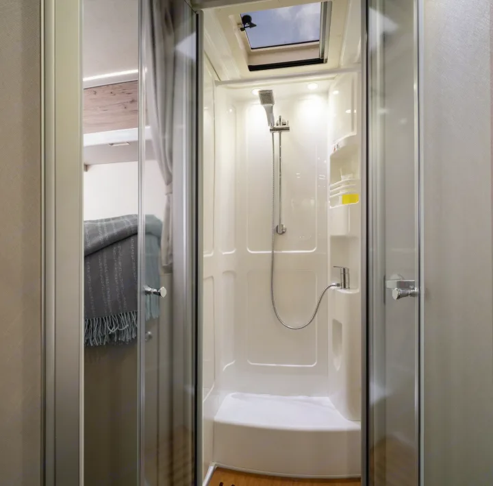 RV rental: View of a compact, white shower stall with skylight & integrated shelves. A peek at the bed area is seen through the glass door.. Hymer Exis I 678 2024