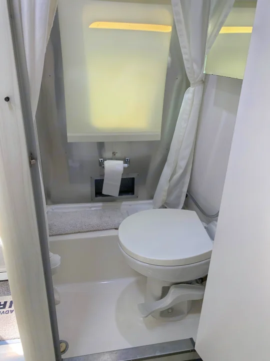 Inside an RV rental: a compact white wet bath featuring a toilet, shower, and curtain for efficient travel.. Airstream Sport 2019