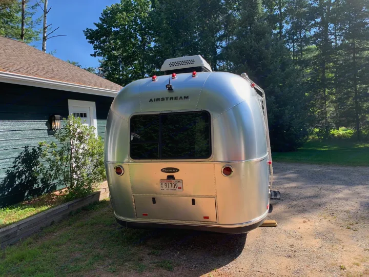 Airstream Bambi travel trailer, often available for rv rental, parked by a house amidst green trees.. Airstream Sport 2019
