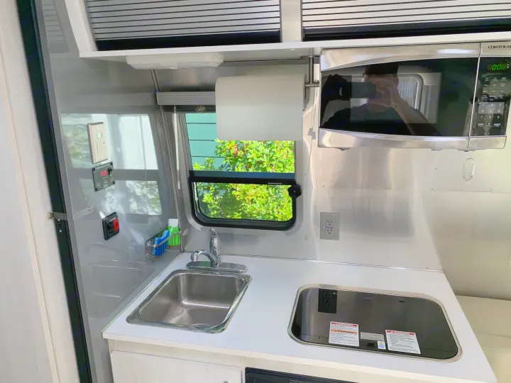 Compact kitchen for an RV rental, featuring a sink, stovetop, microwave, and paper towel holder.. Airstream Sport 2019