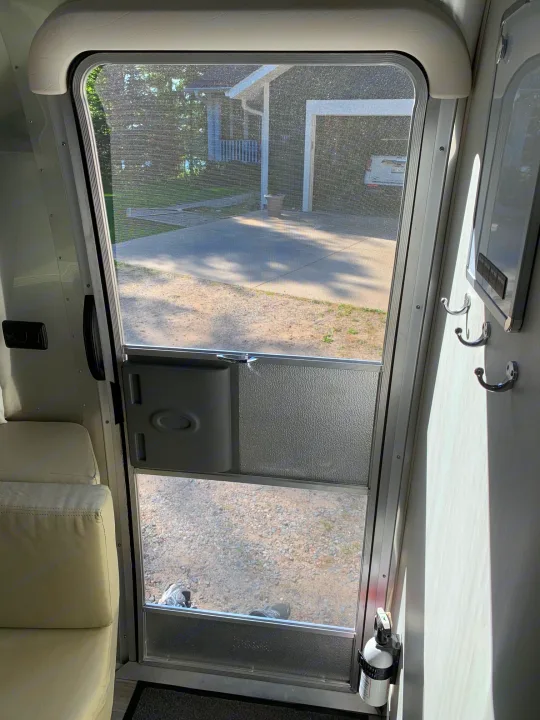 Inside an RV rental looking out through the screen door, revealing a house, trees, and driveway.. Airstream Sport 2019