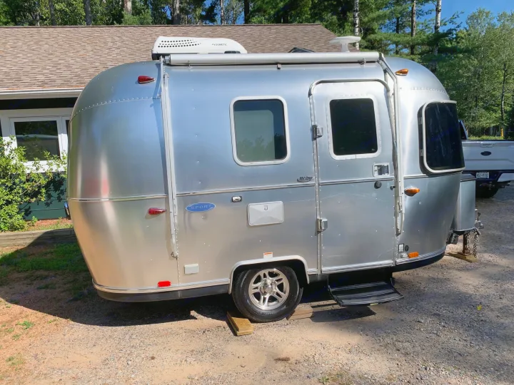 A sleek silver Airstream travel trailer, perfect for an RV rental, is parked on a gravel lot under a clear sky.. Airstream Sport 2019