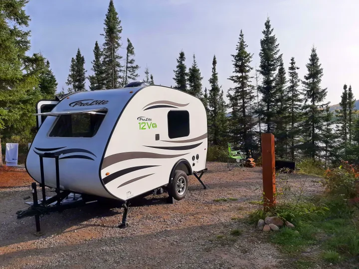 ProLite RV rental on a gravel campsite, surrounded by tall trees with a lake view. Ideal for outdoor travel and camping.. Prolite 12 V 2019