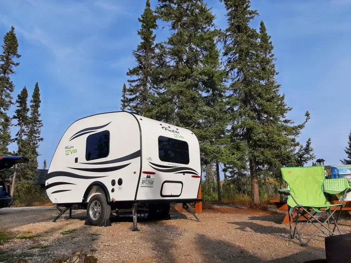 Compact ProLite 12Vq travel trailer at a scenic rv rental campsite with tall trees and outdoor gear.. Prolite 12 V 2019
