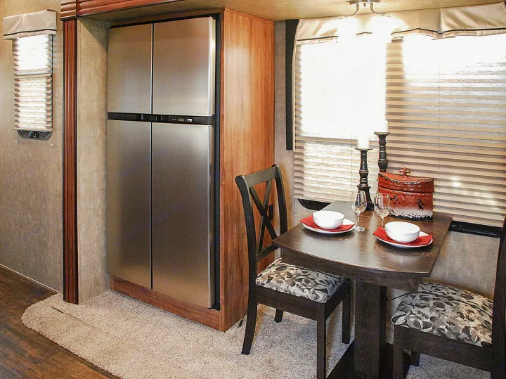 RV rental interior: A compact kitchen and dining area features a stainless steel fridge, a small table set for two, and upholstered chairs.. K-Z Manufacturing Durango 2017