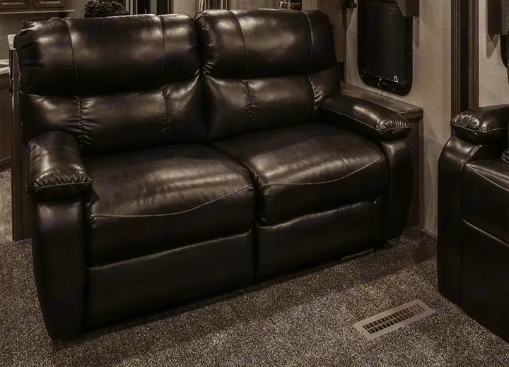 Plush, dark reclining sofa in this RV rental, featuring padded arms & white stitching on gray carpet. Cozy seating.. K-Z Manufacturing Durango 2017