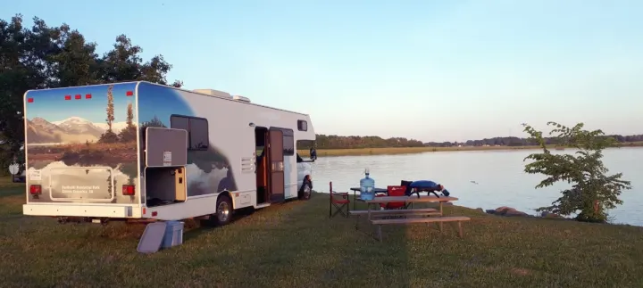Enjoy nature with this RV rental parked by a lake, featuring a grill and picnic area, perfect for camping.. Thor Majestic 2018