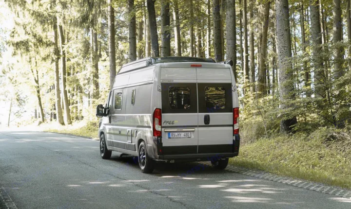 Rear view of a grey camper van on a road winding through a dense, sun-dappled forest, ideal for rv rental.. Hymer FREE 600 CAMPUS 2024
