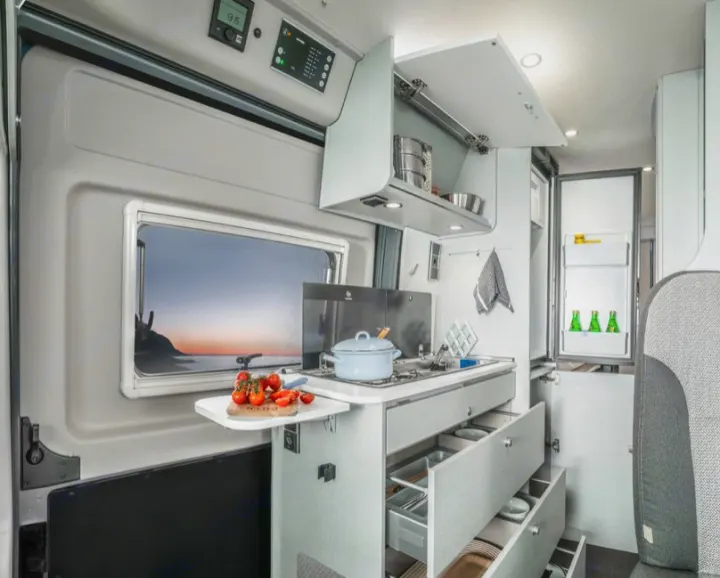 Modern rv rental camper van kitchen with open drawers, fridge, and a window view of a coastal sunset.. Hymer FREE 600 CAMPUS 2024