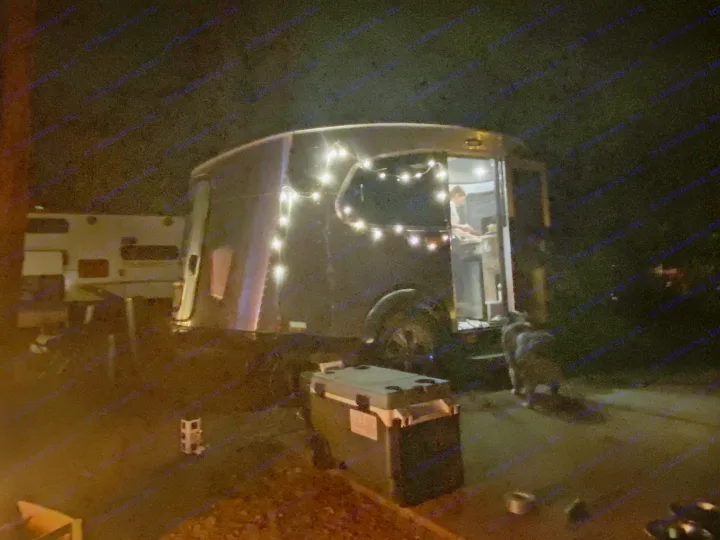 Nighttime RV rental scene: An Airstream-style camper lit with string lights, a person inside, and a dog outside.. Airstream Basecamp 2017