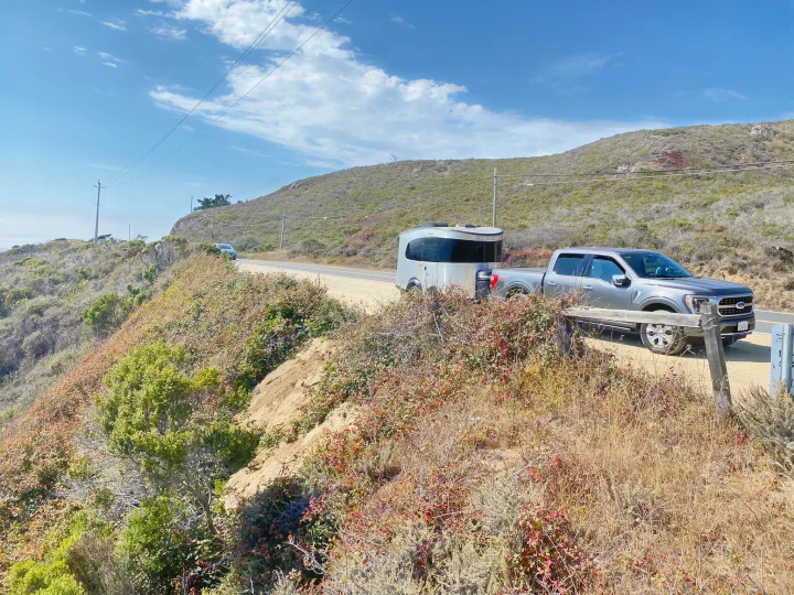 RV rental adventure: a pickup truck tows a sleek travel trailer on a scenic coastal road, perfect for exploring!. Airstream Basecamp 2017
