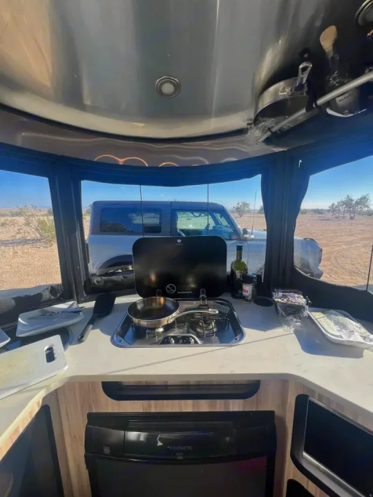 Interior of an RV kitchen with stove, fridge, and desert view. Bronco parked outside. Great for an rv rental adventure!. Airstream Basecamp 2017