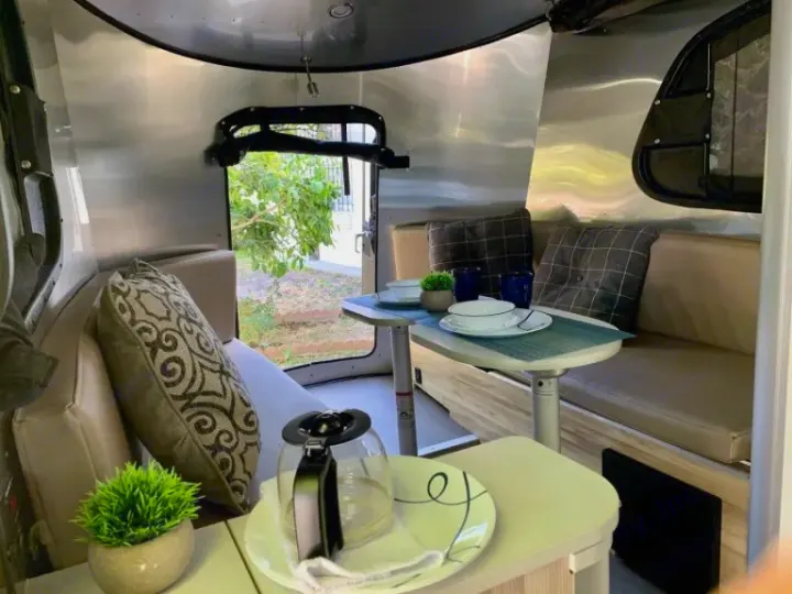 Inviting RV rental interior: shiny silver walls, dining table with place settings, plush seating, & coffee pot.. Airstream Basecamp 2017
