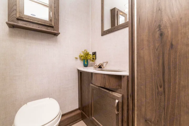 **RV rental** bathroom: A compact space with toilet, sink vanity, & wood-accented cabinets, including an overhead mirror.. CONQUEST 6320D 2024