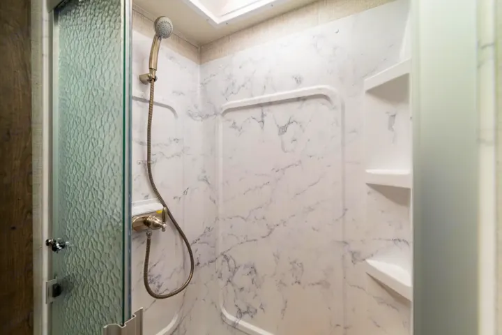 Experience comfort in this RV rental's shower, featuring white marble-patterned walls, a handheld showerhead, and built-in shelves.. CONQUEST 6320D 2024