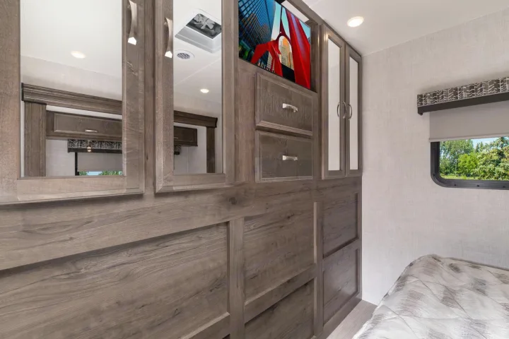 RV rental bedroom with wood-grain cabinets, built-in TV, mirrored doors, and a scenic window view.. CONQUEST 6320D 2024