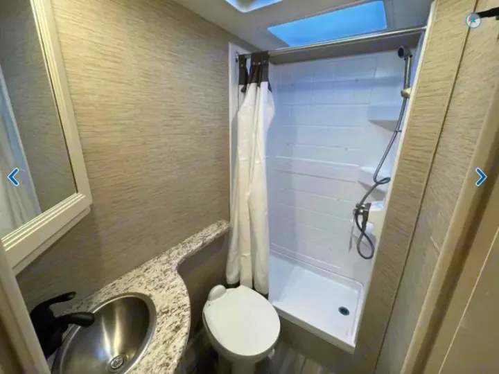 RV rental bathroom: A compact space with a sink, toilet, shower, and skylight. Light, textured walls add a modern feel.. Thor Freedom Elite 2023