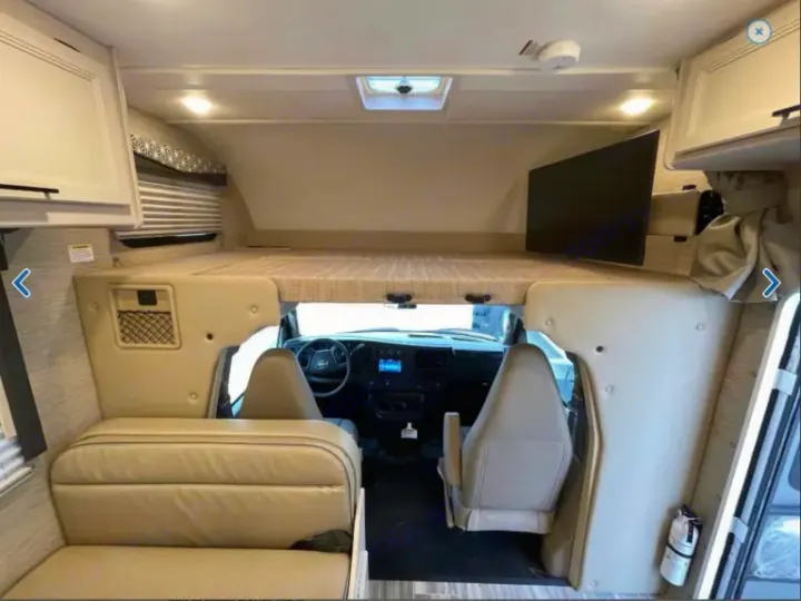 Spacious RV rental interior with over-cab bunk, front cab, and living area featuring a sofa and mounted TV.. Thor Freedom Elite 2023