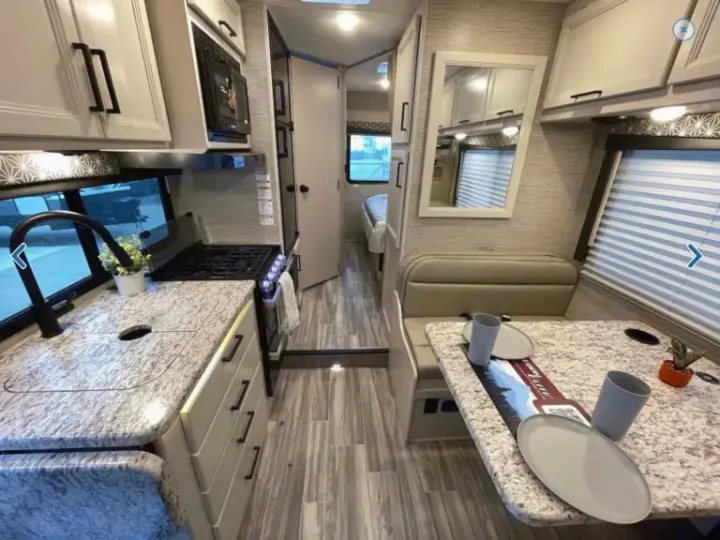 Modern RV rental interior: kitchen with sink/stove, dinette, and rear sleeping area down the hall.. Thor Freedom Elite 2023