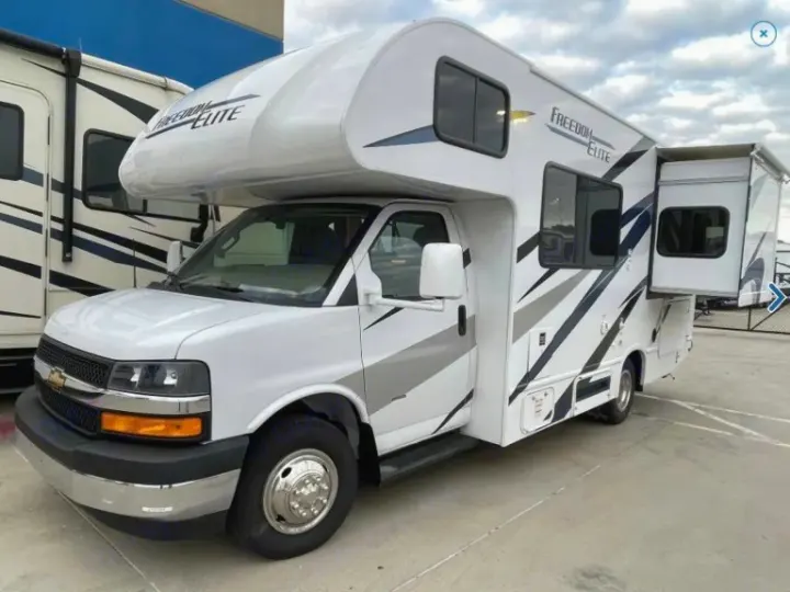 White Class C RV rental, a recreational vehicle with an extended side slide-out, parked on pavement.. Thor Freedom Elite 2023