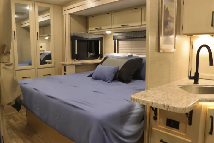 Cozy RV rental interior featuring a comfortable bed with blue sheets and pillows, plus a compact kitchenette with a sink.. Thor Freedom Elite 2023