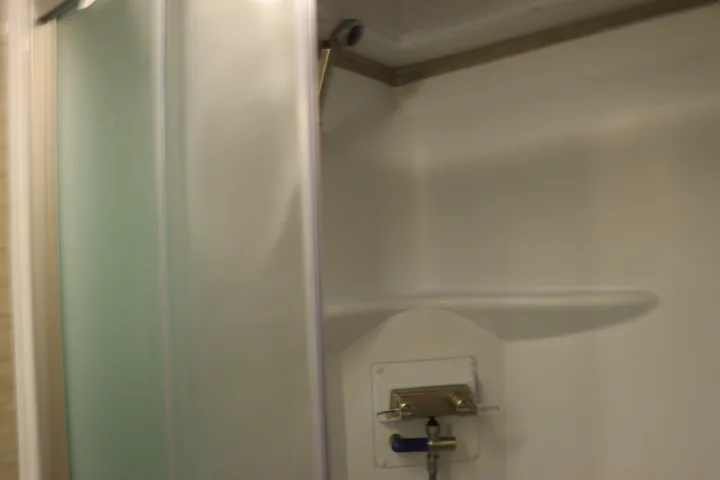 Compact RV rental shower interior with modern controls, a wall-mounted showerhead, and built-in shelf.. Thor Freedom Elite 2023