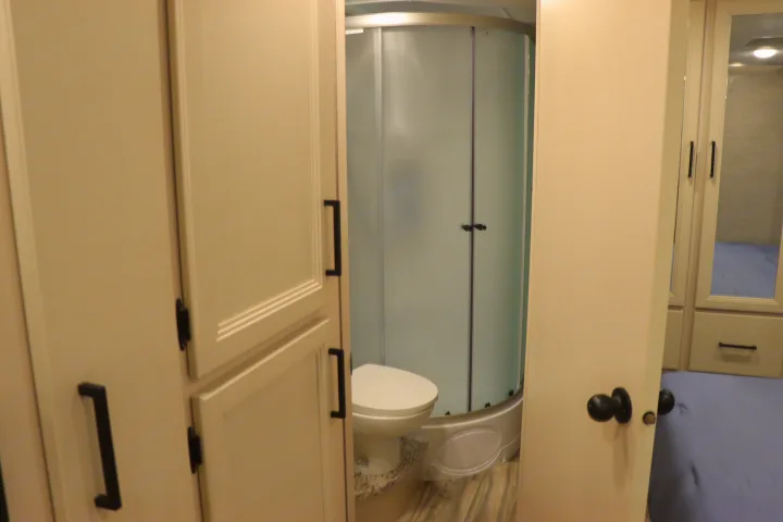 Step inside this RV rental! View of a compact bathroom with a toilet and curved glass shower, next to bedroom entry with mirror closets.. Thor Freedom Elite 2023