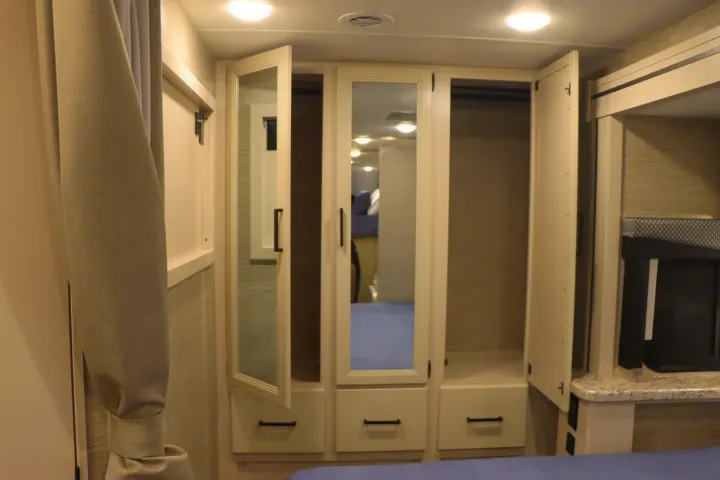 RV rental interior: compact bedroom with white mirrored wardrobe, drawers, and an entertainment nook next to the bed.. Thor Freedom Elite 2023
