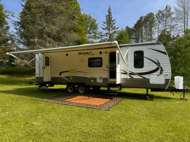 An RV rental, a white travel trailer, extends its awning over an outdoor rug on lush green grass for camping.. Keystone Hideout LHS 2014