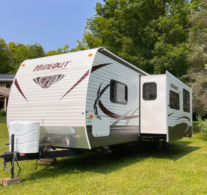 A white rv rental travel trailer, with its side expanded, is parked on a sunny grassy lawn by trees.. Keystone Hideout LHS 2014