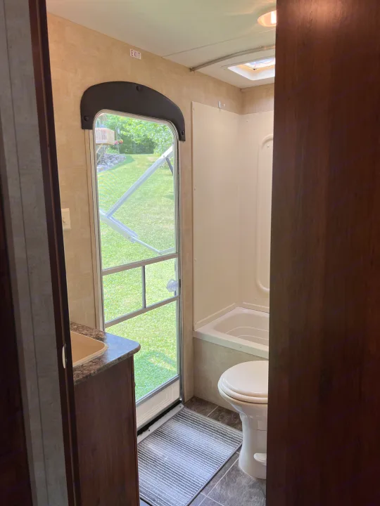 View inside an RV rental bathroom, showing a tub/shower, toilet, sink, and the screen door leading to a grassy outdoor area.. Keystone Hideout LHS 2014