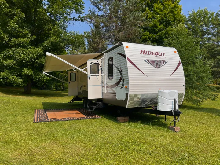 White Hideout travel trailer with awning & outdoor rug on green grass. Ideal RV rental for a relaxing campsite stay.. Keystone Hideout LHS 2014