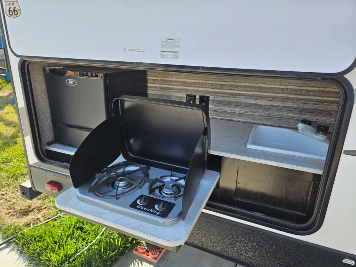 Outdoor kitchen in an rv rental, featuring a FlameKing stove, sink, and mini-fridge. Ideal for convenient camping.. Heartland RVs North Trail 2019