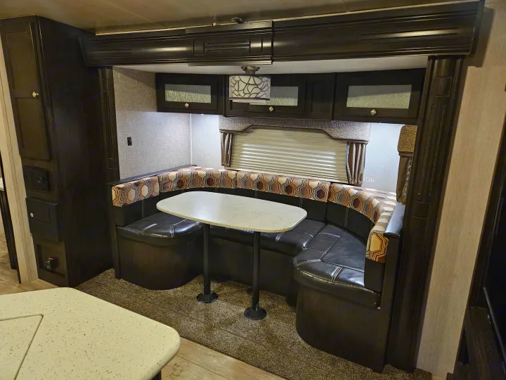 RV rental interior: U-shaped dinette with patterned cushions, black seating, an oval table, and dark overhead cabinets.. Heartland RVs North Trail 2019