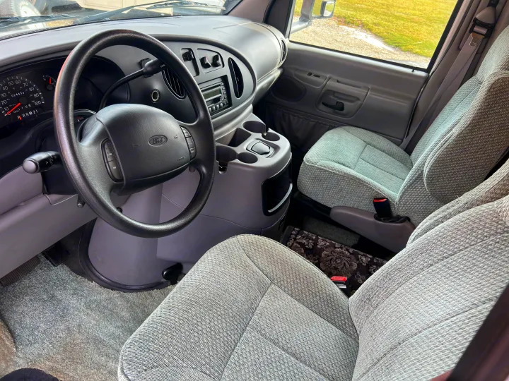 Inside a Ford van, likely an RV rental, featuring the cockpit with steering wheel, dashboard, radio, and comfortable seats.. Winnebago Minnie 2002