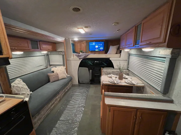 Step inside this RV rental, showcasing a full living area with couch, dining booth, and overhead bunk for comfortable travel.. Winnebago Minnie 2002