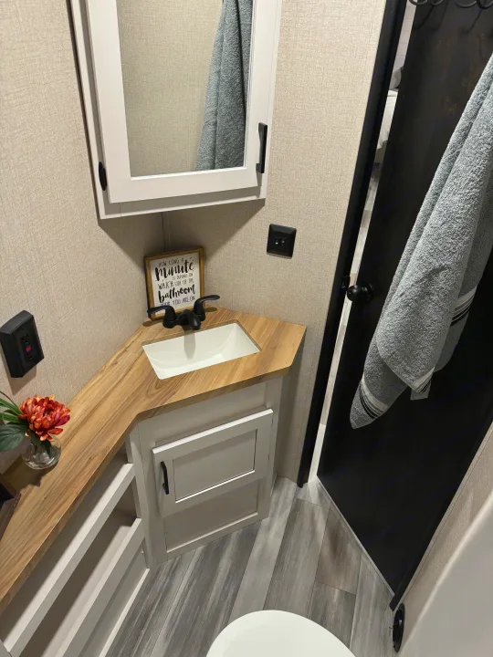 RV rental bathroom with a wood vanity, white sink, mirrored medicine cabinet, toilet, and storage. Compact and functional space for travel.. Starcraft 26BHS 2024