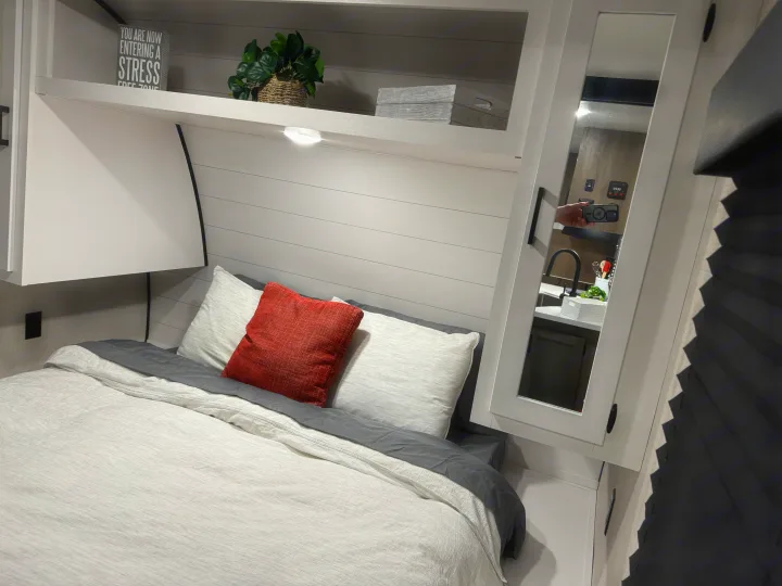 Cozy RV rental bedroom features a comfy bed, overhead shelves with decor, and a mirrored cabinet reflecting the interior.. Starcraft 26BHS 2024