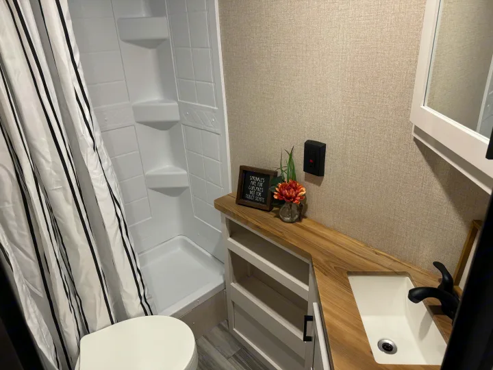 Clean RV rental bathroom with a compact shower, striped curtain, toilet, and vanity with sink. Light, textured walls enhance the functional travel space.. Starcraft 26BHS 2024